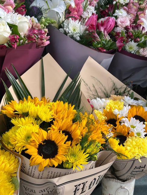 Multiple bouquets of fresh flowers arranged for delivery include a prominent bouquet of bright yellow sunflowers with dark centers, complemented by small white daisies and yellow chrysanthemum accents